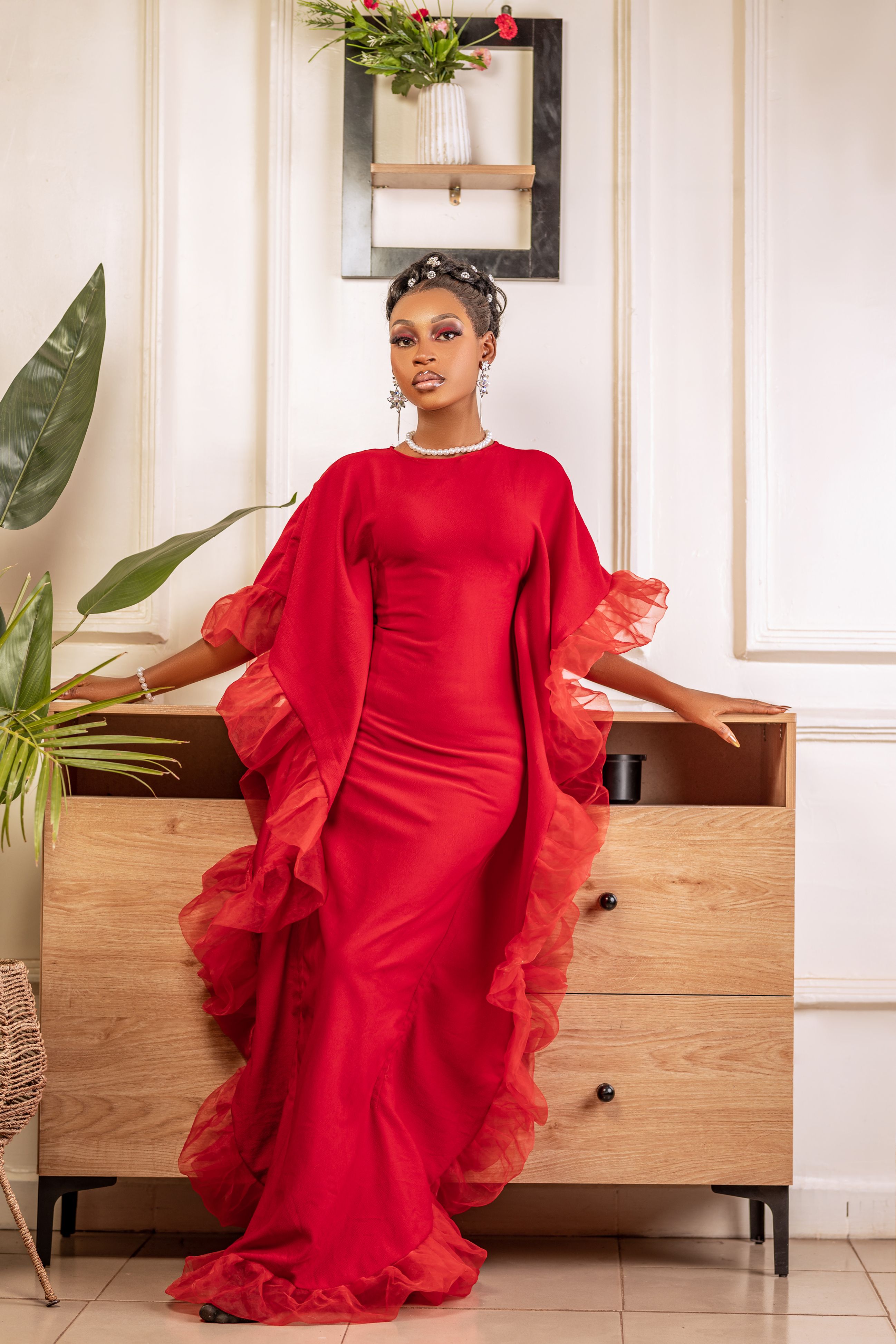 A woman in a floor-length red gown with sheer organza ruffle cape sleeves and a pearl necklace